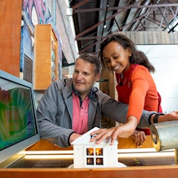 A child and a man smiling while interacting with a house exhibit inside the Engine Shed