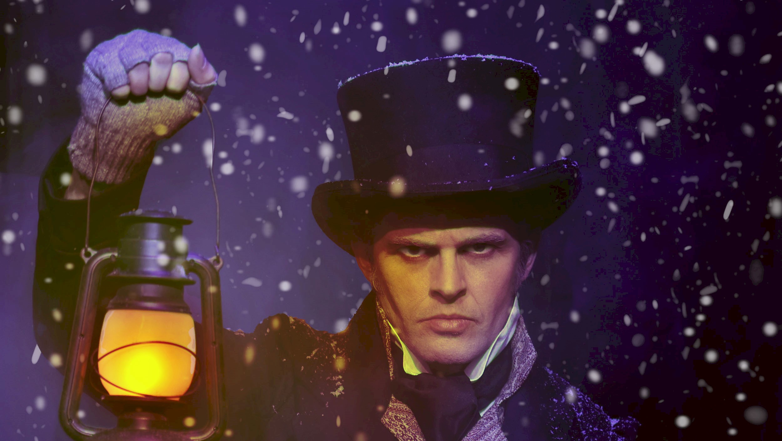 A man dressed as Ebeneezer Scrooge looking sternly at the camera holding up a lantern