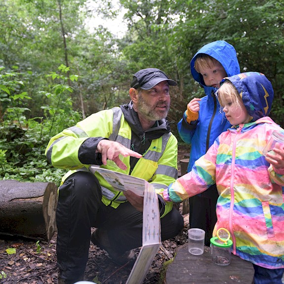 Two children with a Ranger all wearing waterproofs and looking at bugs