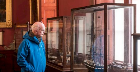 A man looking at a model ship in a glass case in the vast convening room at Trinity House