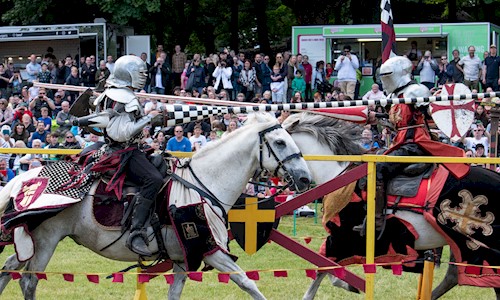 Costumed performers on horses galloping towards each other with jousts