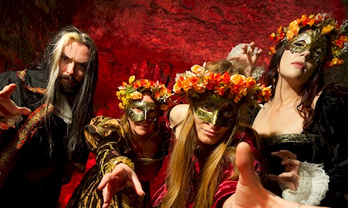 Four re-enactors, three of them wearing floral crowns and gold facemasks, and enticing you towards them with their hands