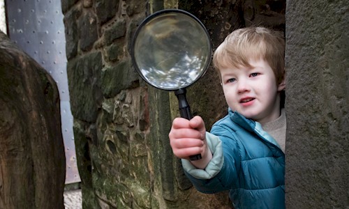 Child in a blue coat looking for Easter egg clues with a magnifying glass at Craigmillar Castle