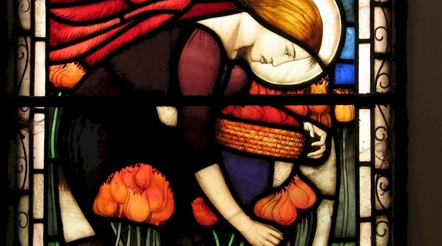 A stained glass window featuring a woman picking orange tulips 