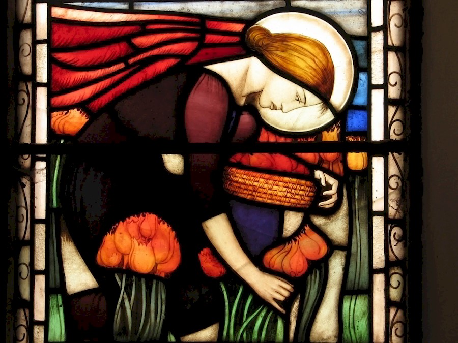 A stained glass window featuring a woman picking orange tulips 
