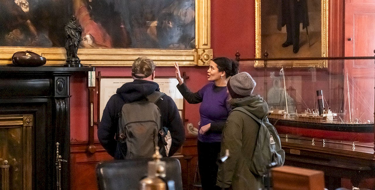 Three people in a room painted in a rich red colour and surrounded by maritime memorabilia