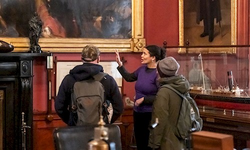 Three people in a room painted in a rich red colour and surrounded by maritime memorabilia
