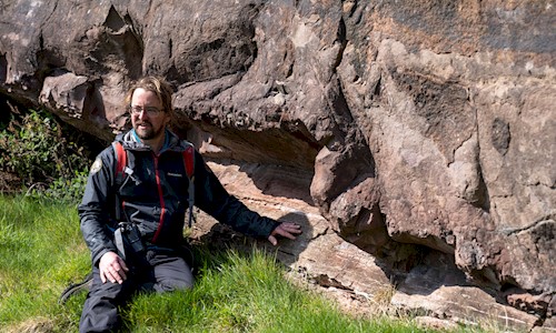 A Park Ranger sitting on grass touching some stone below Salisbury Crags 