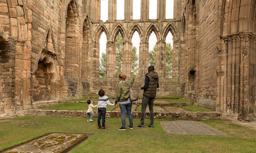 Two adults and two children looking up at the ruins of Elgin cathedral