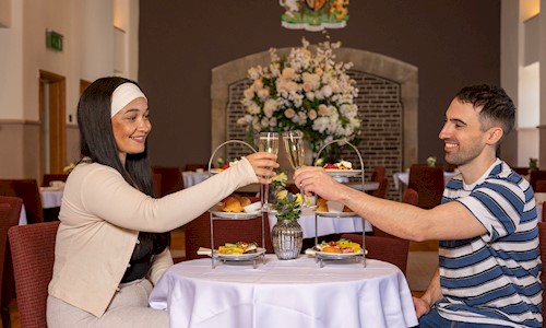 Two people clinking champagne glasses and enjoying afternoon tea