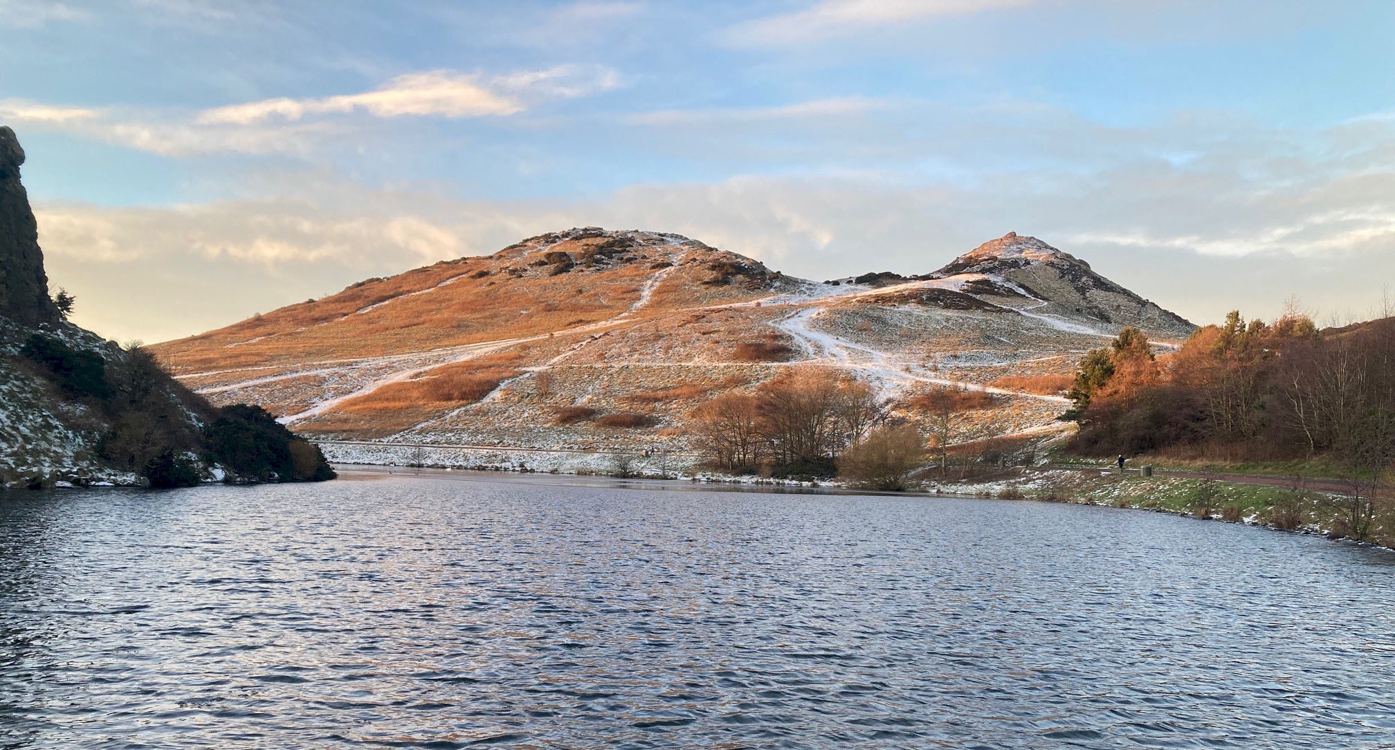 A loch with hills in the background with a scattering of snow