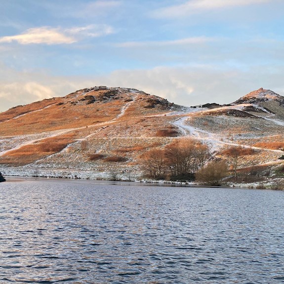 A loch with hills in the background with a scattering of snow
