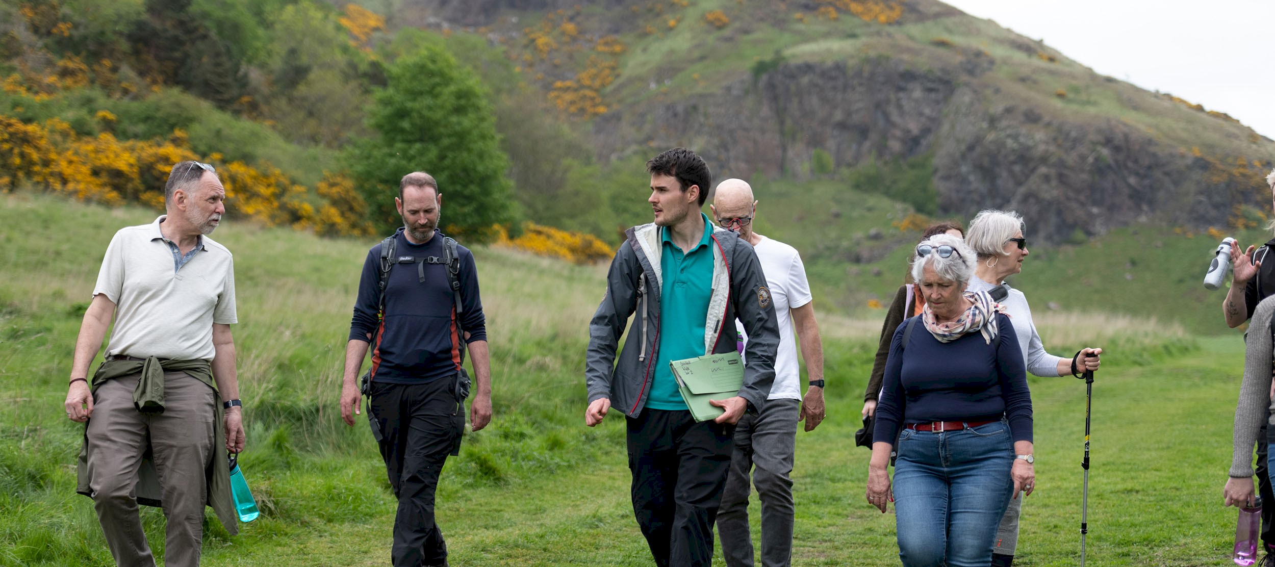 A group of adults walking on a hill on a bright day with a Ranger leading the tour