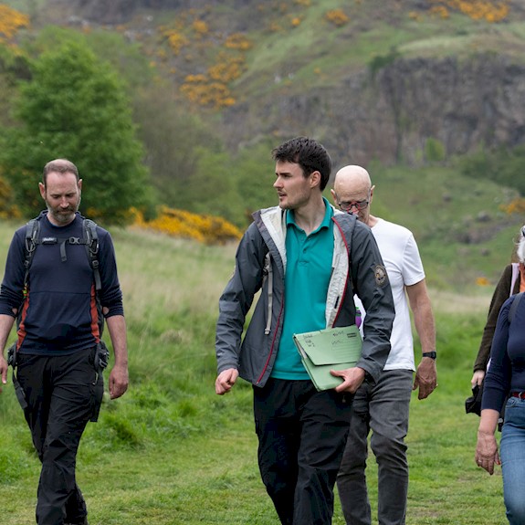 A group of adults walking on a hill on a bright day with a Ranger leading the tour