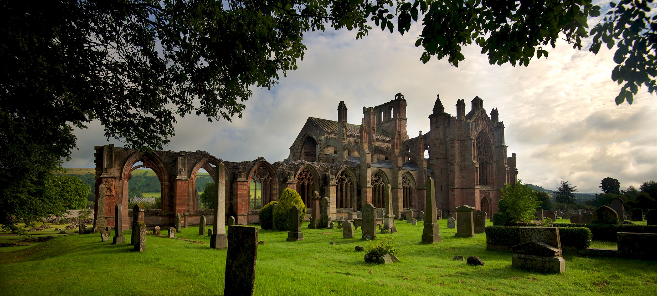 Beautiful exterior view of an historic abbey with surrounded with grass, trees and gravestones 