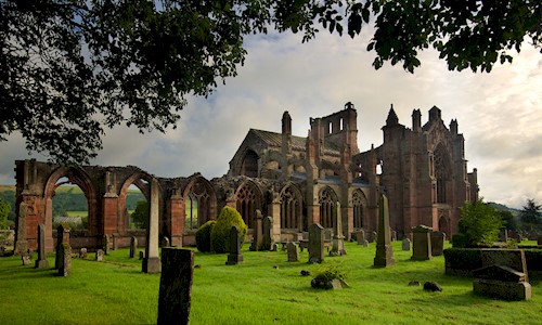 Beautiful exterior view of an historic abbey with surrounded with grass, trees and gravestones 