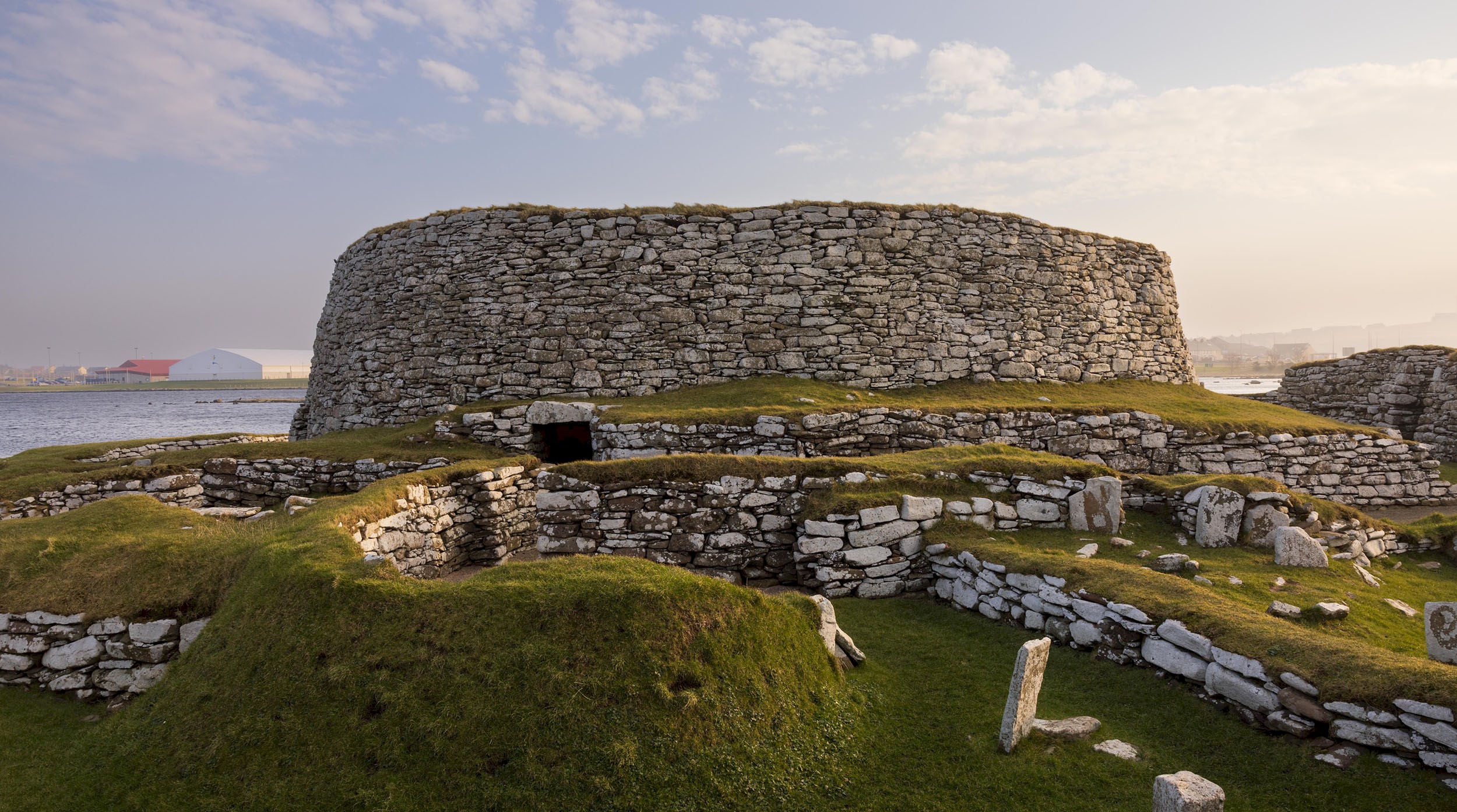 A broch with the sun shining over it and Clickimin Loch in the background
