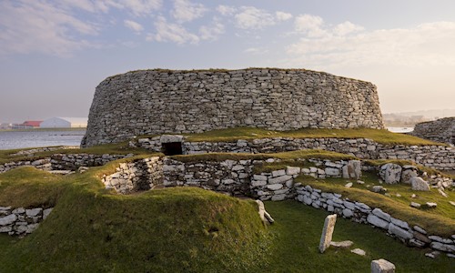 A broch with the sun shining over it and Clickimin Loch in the background