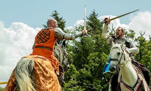 Two knights on horses taking part in a joust and wielding their swords at each other