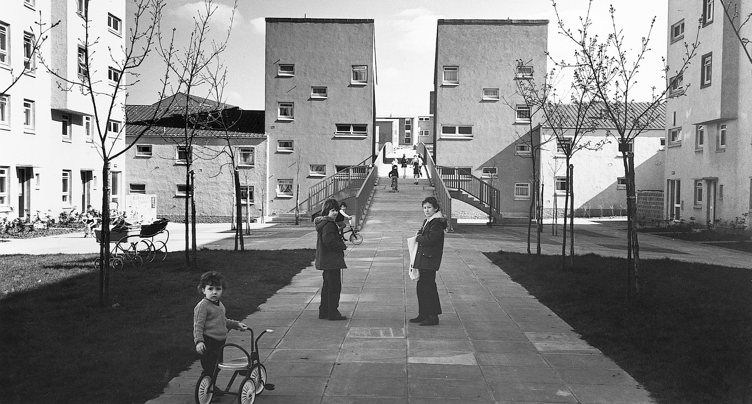 black and white picture of tenement blocks and children playing on bikes and with prams