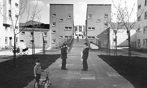 black and white picture of tenement blocks and children playing on bikes and with prams