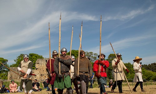 Costumed performers dressed as soldiers carrying bow and arrows and spears in the grounds of a ruin
