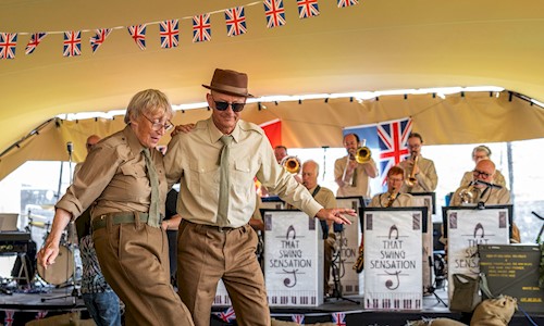 Two people in military uniform under a large gazebo dancing along to a swing band who are also in military uniform 