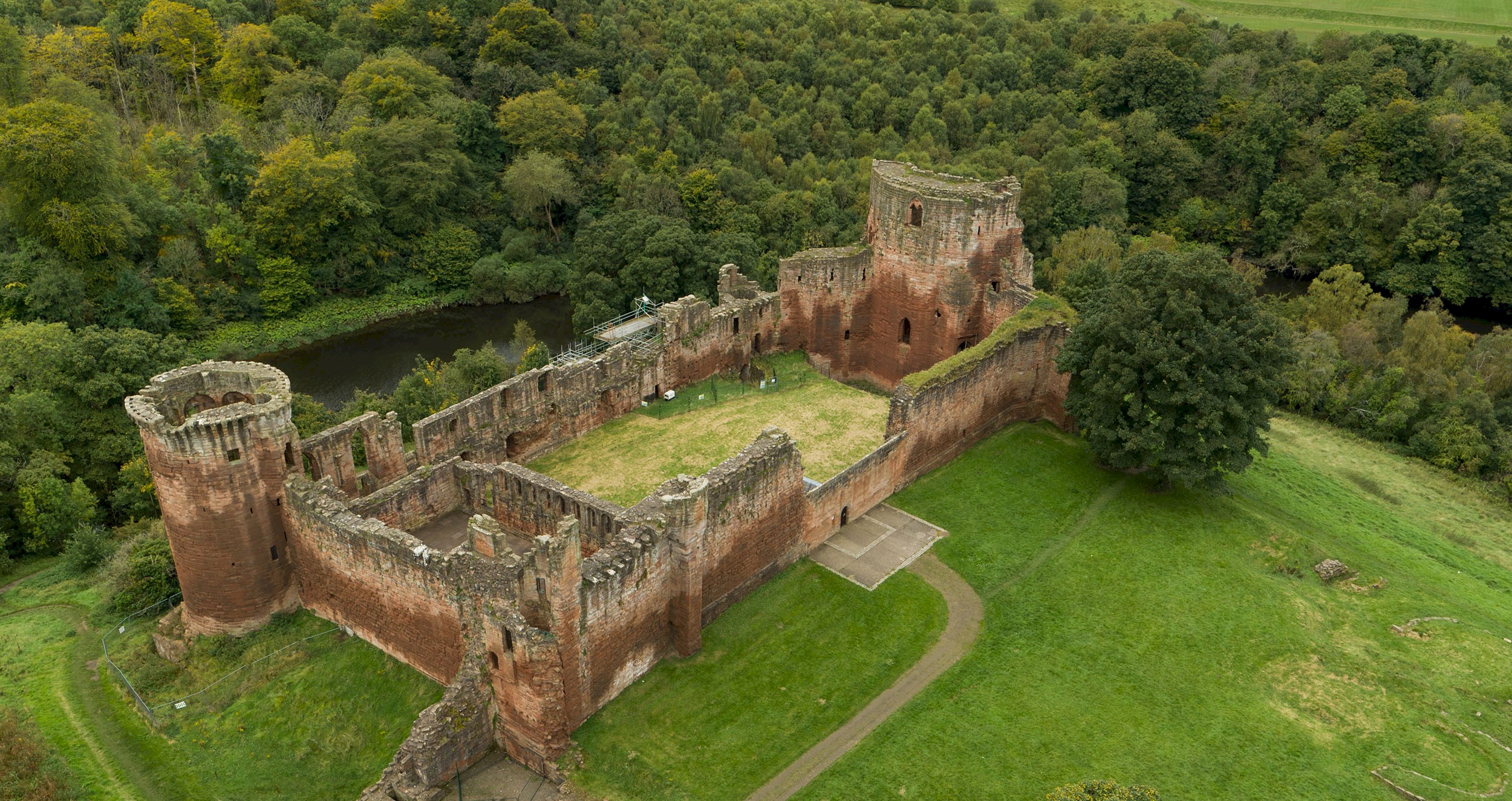 An aerial view of castle ruins, surrounded by grass and trees and a path leading up to the entrance