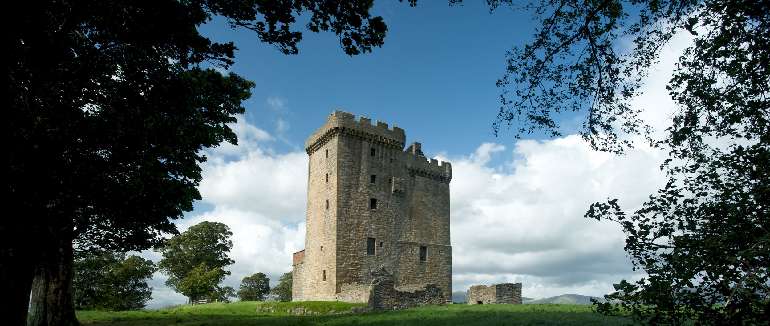 Exterior view of a tower surrounded by lush green grass, blue skies and trees