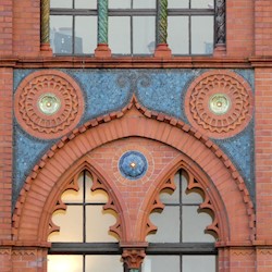 An ornate sequence of red and blue tiles on the outside wall of a building, with windows above and below.
