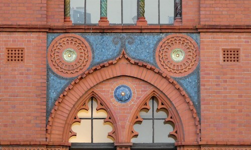 An ornate sequence of red and blue tiles on the outside wall of a building, with windows above and below.