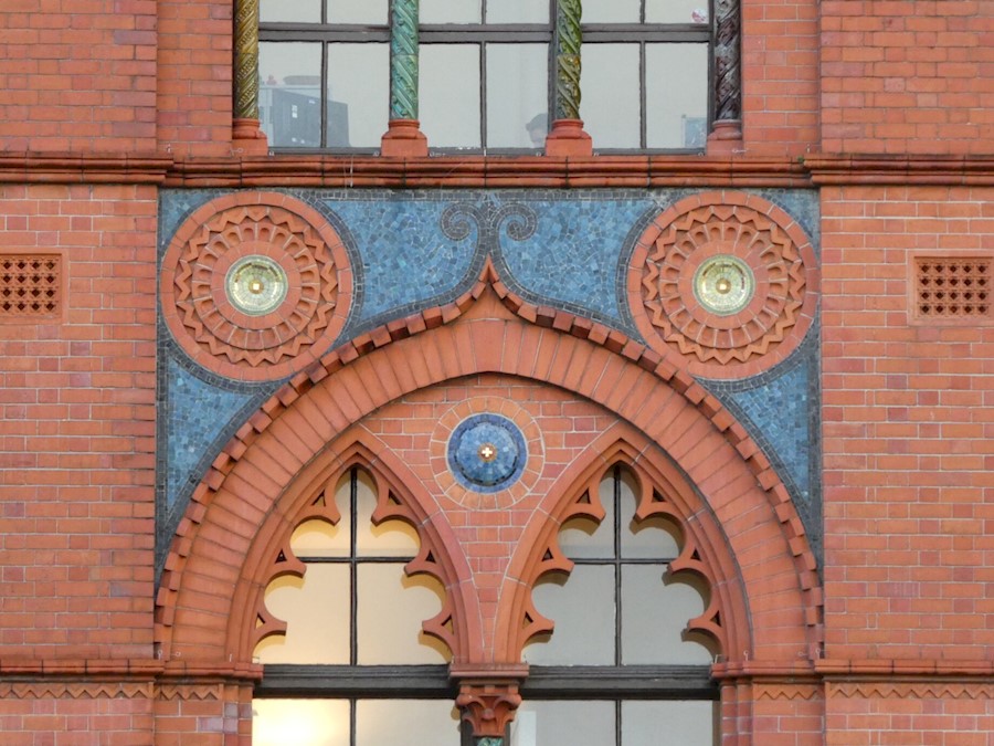 An ornate sequence of red and blue tiles on the outside wall of a building, with windows above and below.