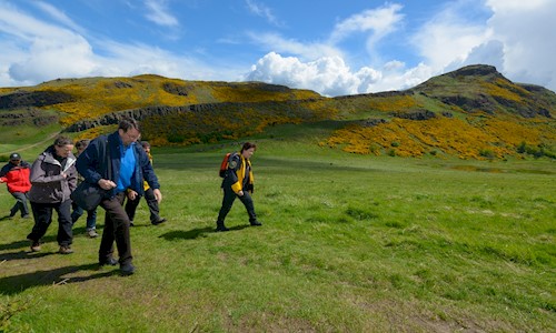 A group of people in outdoor wear follow a Ranger over a hill