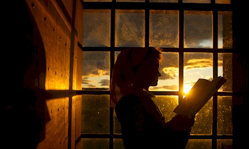 Costumed performer reading book by a sunset framed window at Stirling Castle
