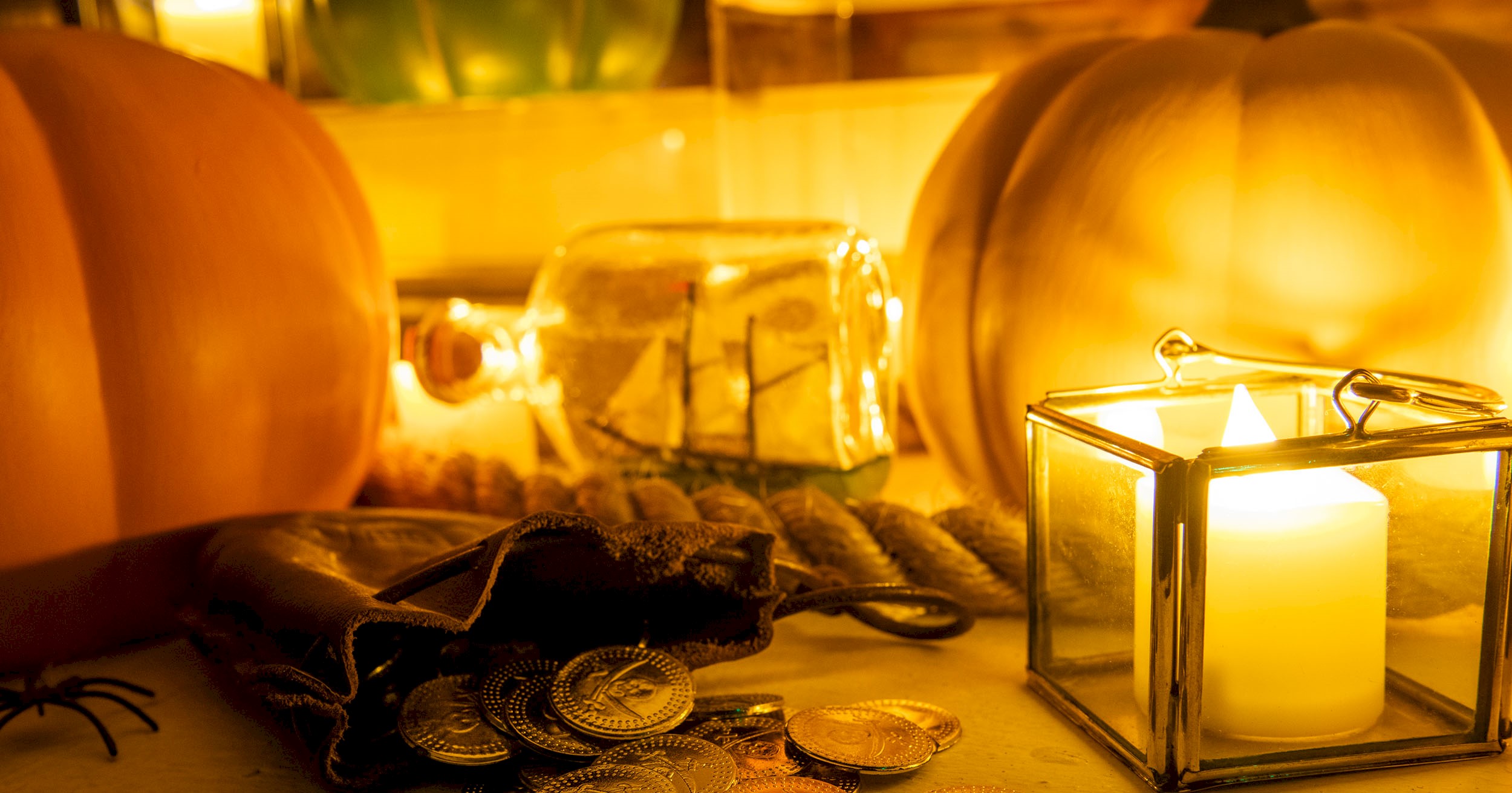 Two large pumpkins, a lit candle, a bag of gold coins and a ship in a bottle