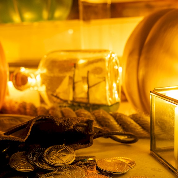 Two large pumpkins, a lit candle, a bag of gold coins and a ship in a bottle