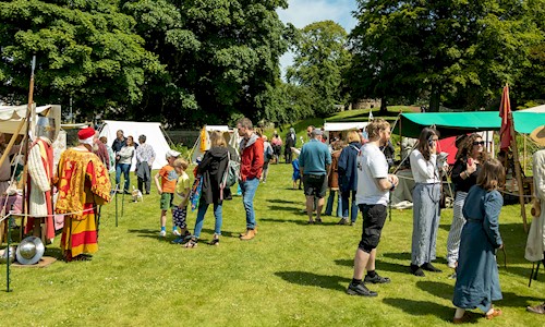 Visitors walking round a medieval encampment in the glorious sunshine talking to the tradespeople at their stalls 