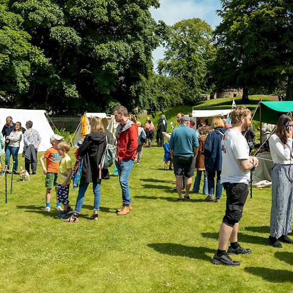 Visitors walking round a medieval encampment in the glorious sunshine talking to the tradespeople at their stalls 