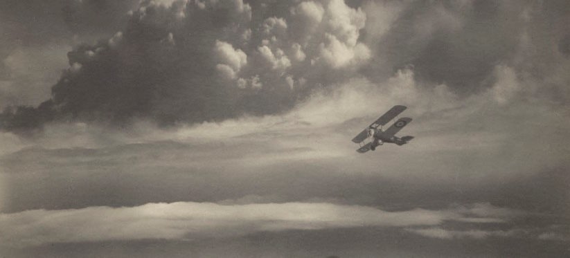 A black and white picture of a Vintage Biplane flying over a castle and some hills