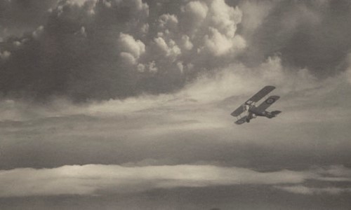 A black and white picture of a Vintage Biplane flying over a castle and some hills