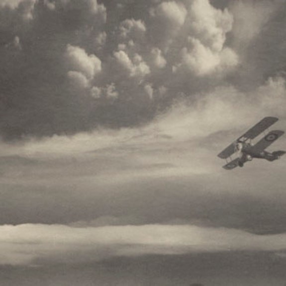 A black and white picture of a Vintage Biplane flying over a castle and some hills