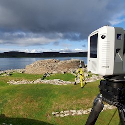A digital surveying camera mounted on a tripod overlooking a historic burial site next to the sea.