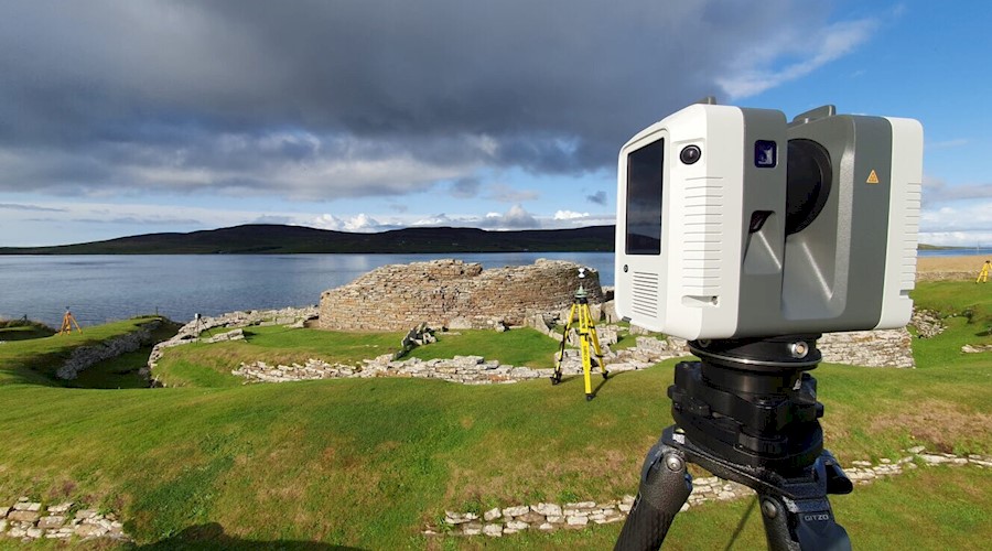 A digital surveying camera mounted on a tripod overlooking a historic burial site next to the sea.
