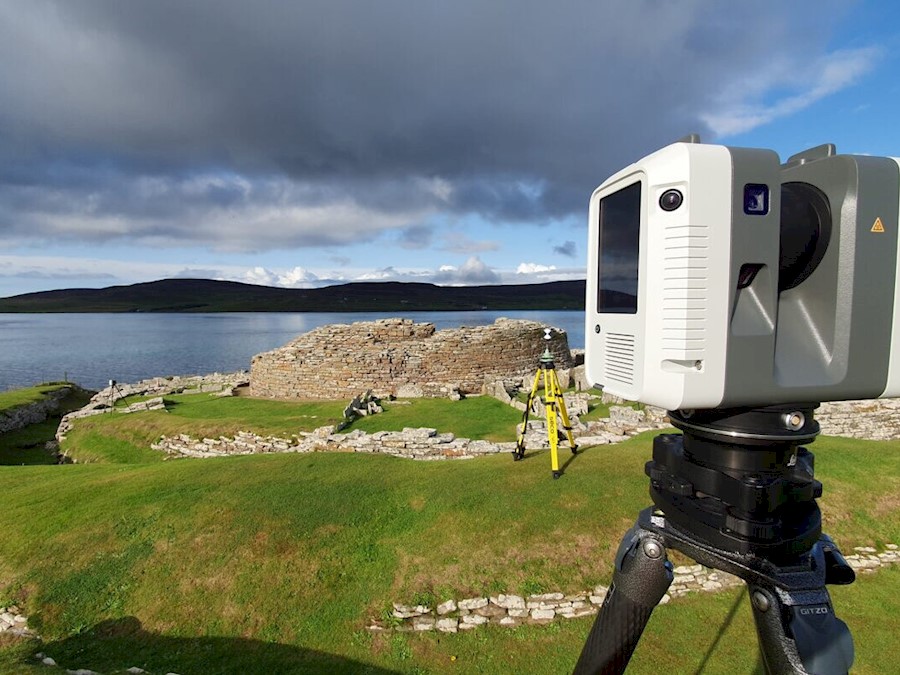 A digital surveying camera mounted on a tripod overlooking a historic burial site next to the sea.