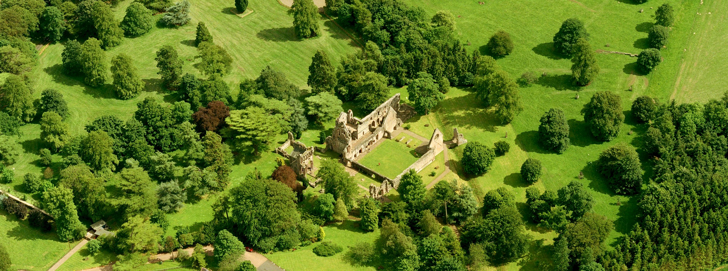 Aerial view of a ruined abbey with lots of green grass and trees surrounding it