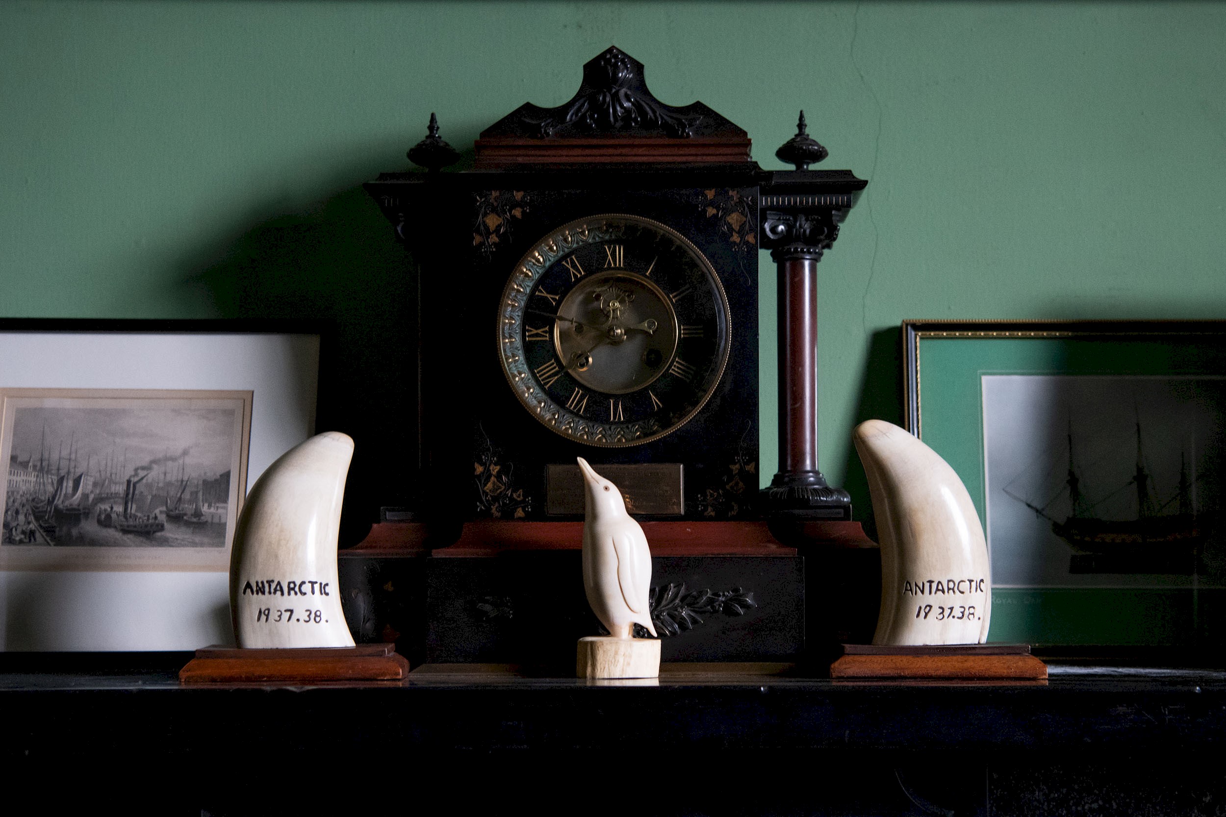 An old clock on a fireplace, along with a whale tooth and a penguin carving