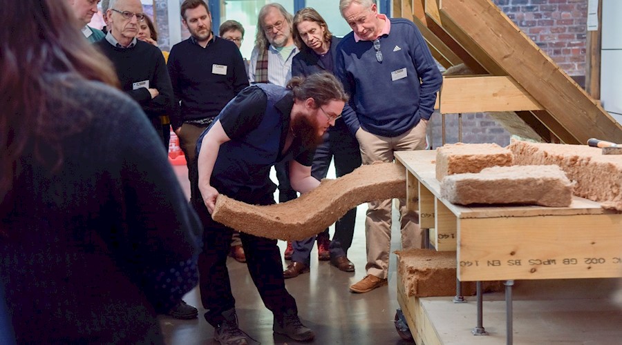 A person pushing insulation into a wooden display stand, demonstrating building insulation to a group of people