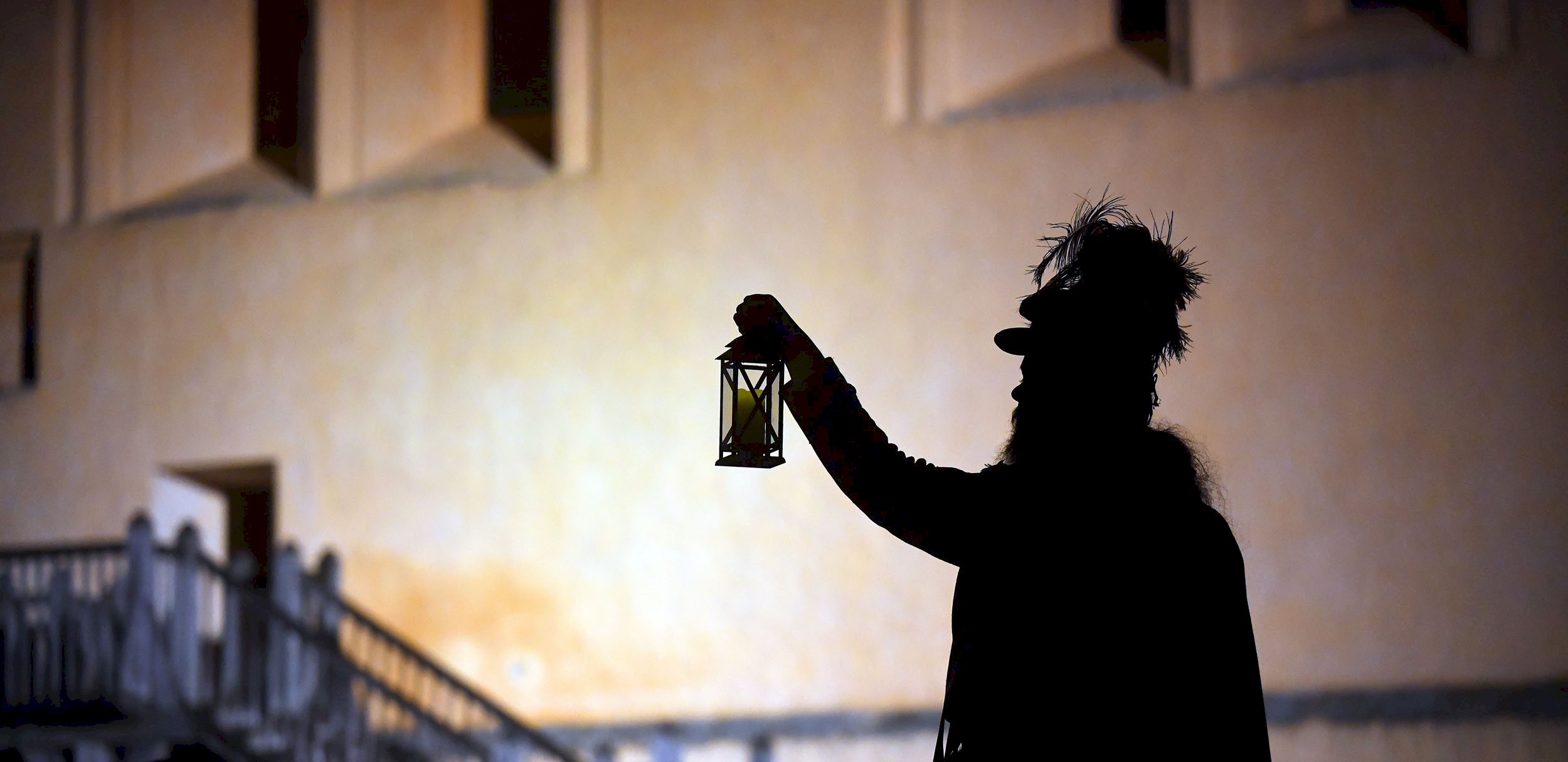 Silhouette of a man holding a lantern up with his right hand 