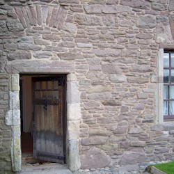 A timber door and window set into the side of a historic castle wall, made up of many intricate stones and shaped bricks.