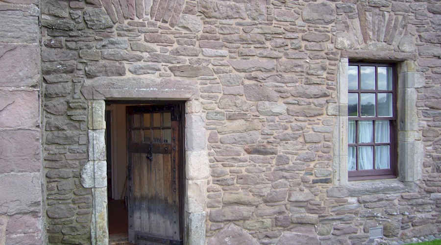 A timber door and window set into the side of a historic castle wall, made up of many intricate stones and shaped bricks.